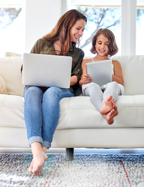 Young mother doing schoolwork on the couch next to her daughter